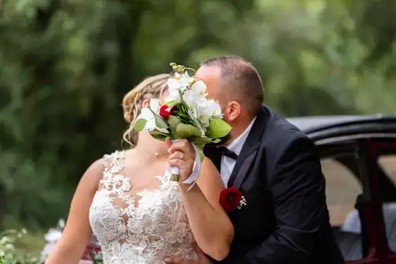 un couple de mariés se cachent derrière leur bouquet pour s'embrasser